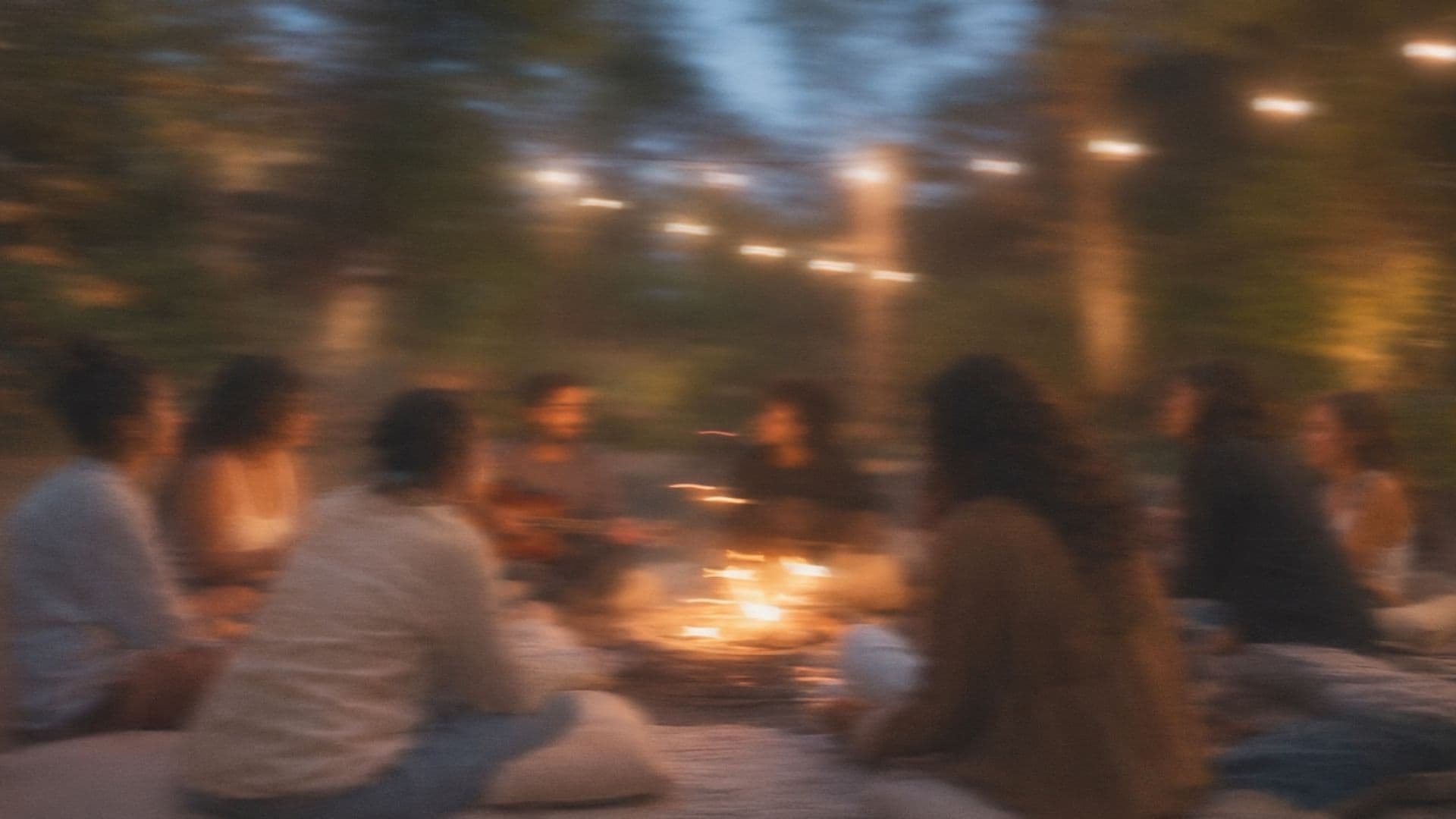 A community circle around a fire, string lights overhead